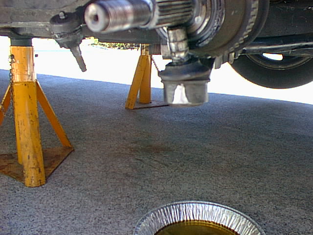 Car on yellow jack stands with foil pan of drained fluid on the concrete below