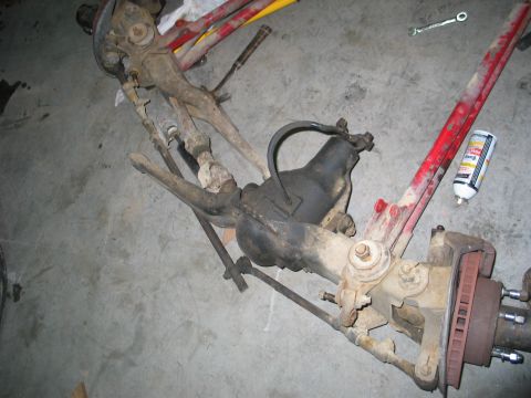 1984 Ford Bronco - A disassembled front axle assembly, likely from an older vehicle, rests on a concrete surface with tools nearby.
