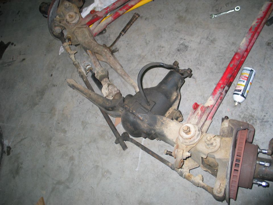 Front axle assembly with red painted components and a can of spray lubricant on a concrete floor