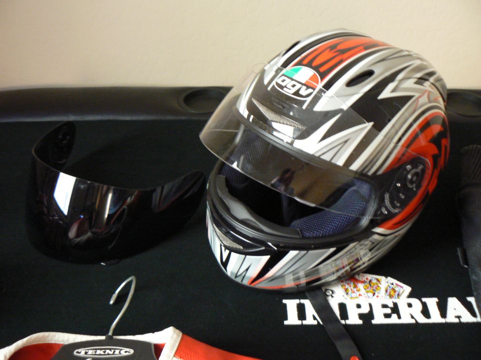 Motorcycle helmet with visor next to it, on a black surface. Some playing cards are visible underneath