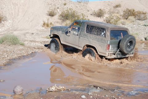 1982 Ford Bronco - This Ford Bronco is navigating a muddy obstacle, kicking up water and dirt.