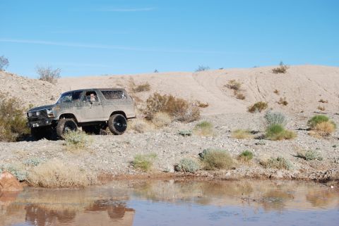 1982 Ford Bronco - Ford Bronco navigates a desert terrain with dry brush and a small body of water.