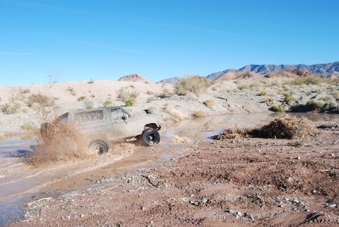 1982 Ford Bronco - A 4x4 vehicle navigates a muddy off-road trail under a clear blue sky.