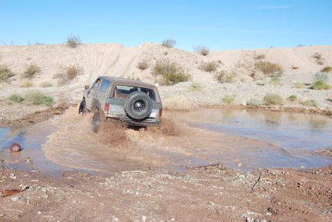 1982 Ford Bronco - Ford Bronco navigates a muddy terrain, kicking up water and dirt.