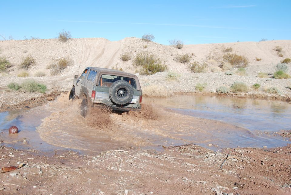 1980s Ford Bronco splashing through a mud puddle off-road