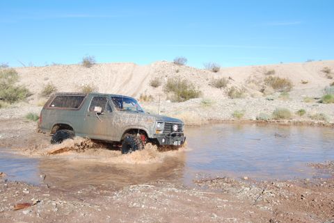 1982 Ford Bronco - This classic Ford Bronco navigates a muddy obstacle in a dry, arid environment under a clear blue sky.