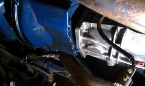 1990 Ford Mustang - Underside view of vehicle transmission and exhaust components, including a blue housing and oxygen sensor.