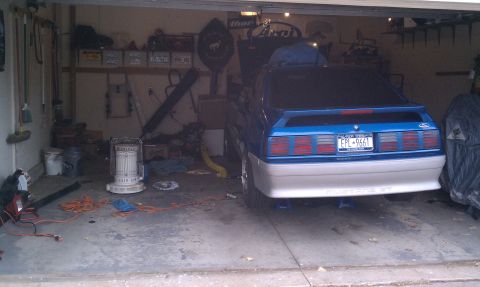 1990 Ford Mustang - This 1990 Ford Mustang GT is parked in a garage, showing its distinctive blue and white paint scheme and rear spoiler.