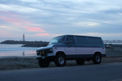 1989 Ford Bronco - A two-tone van sits by the ocean at dusk, with a lighthouse visible on the horizon.
