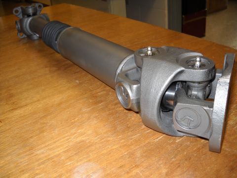 1991 Ford Bronco - A driveshaft assembly, likely for a truck or SUV, is shown on a wooden surface. The part features U-joints and a protective rubber boot.