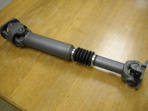 1991 Ford Bronco - A driveshaft with a rubber bellows boot and universal joints is shown on a wooden surface.