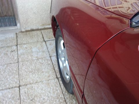 1998 Ford Crown Victoria - Close-up of a red car's fender and wheel, showing the side profile.