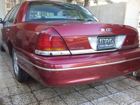 1998 Ford Crown Victoria - The rear of a red Ford Crown Victoria is shown, with a license plate and 'Crown Victoria' badging visible.