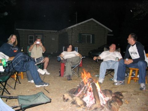 1986 Ford Bronco - A group of people enjoy a campfire outside a rustic cabin.