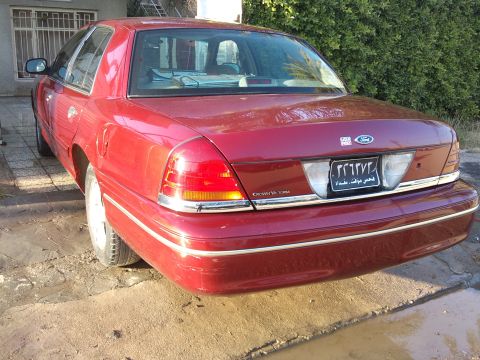 1998 Ford Crown Victoria - Rear view of a red 1998 Ford Crown Victoria sedan, showing its distinctive taillights and chrome accents.