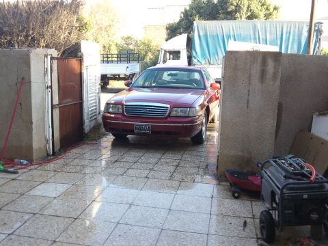 1998 Ford Crown Victoria - A red 1998 Ford Crown Victoria is parked in a driveway, with a truck visible in the background.