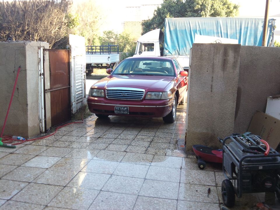 Red 1998 Ford Crown Victoria parked in a driveway, front view. The car has orange side mirrors and a license plate