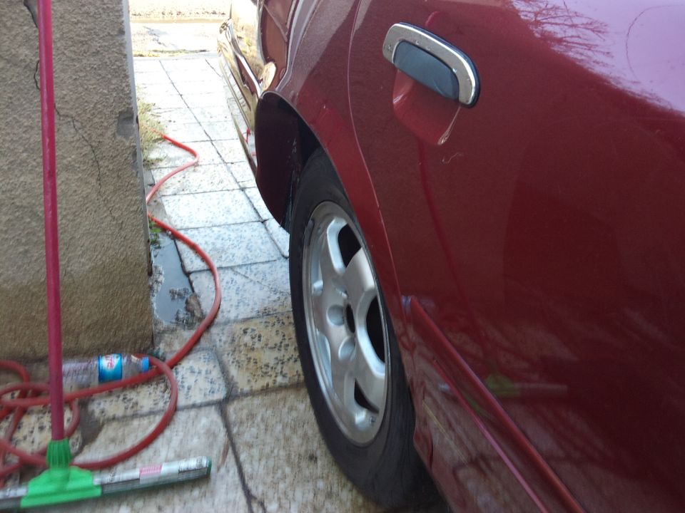 Red car side panel, door handle, and wheel. Red hose and cleaning tools on wet pavement