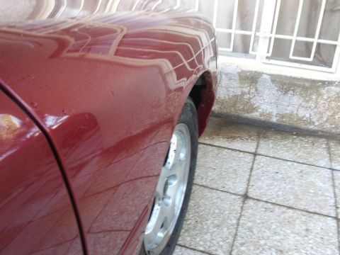 1998 Ford Crown Victoria - A portion of a red vehicle is shown, focusing on the rear fender and wheel area.