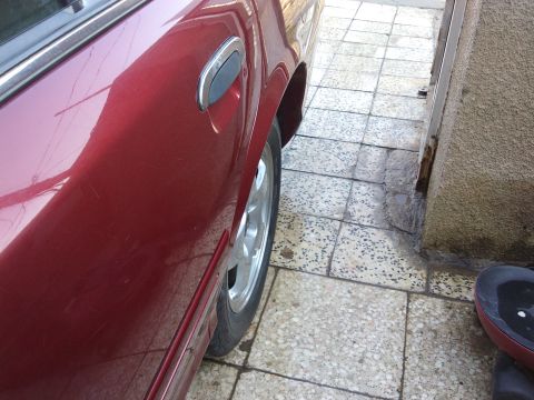 1998 Ford Crown Victoria - The side profile of a red 1998 Ford Crown Victoria, showing the door handle and wheel.