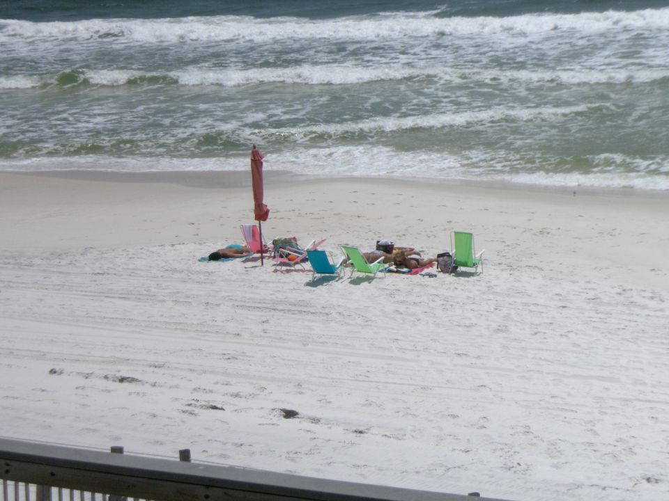 People sunbathing on a beach with chairs and an umbrella near the ocean waves