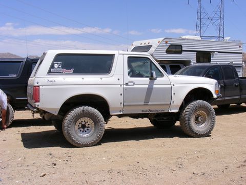 1996 Ford Bronco - A white lifted Ford Bronco with off-road tires is parked next to a trailer and another truck.