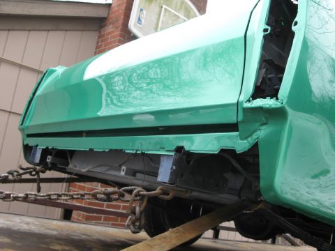 1971 Ford Ranchero - The rear section of a green vehicle is being transported on a trailer, showing exposed undercarriage and bodywork.