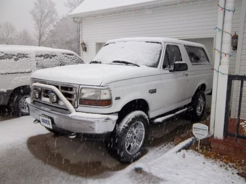 1995 Ford Bronco - A white Ford Bronco sits covered in snow next to a house.
