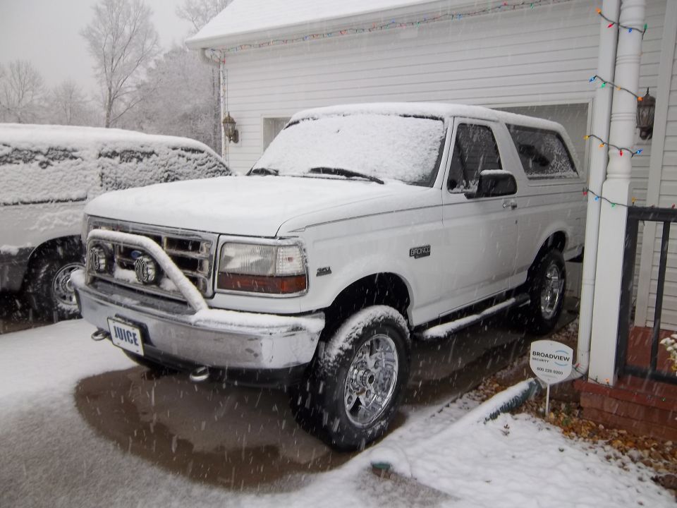 White Ford Bronco with chrome wheels and a brush guard parked in the snow