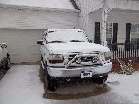 1995 Ford Bronco - A white 1995 Ford Bronco is parked in front of a house during a snowstorm, a chrome bull bar and a custom license plate.
