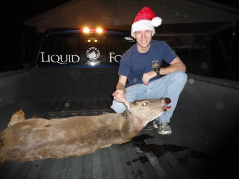 2006 Dodge 2500 - A man in a Santa hat poses with a deer in the back of a blue pickup truck.
