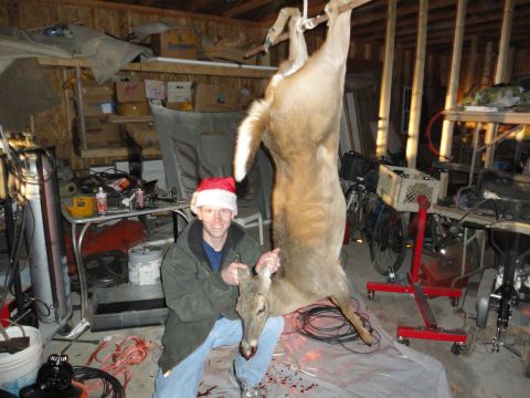 2006 Dodge 2500 - A man in a Santa hat poses with a deer carcass hanging in a cluttered garage.