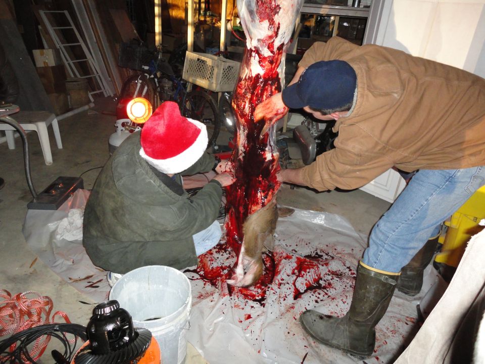 Two people butchering a deer carcass in a garage.