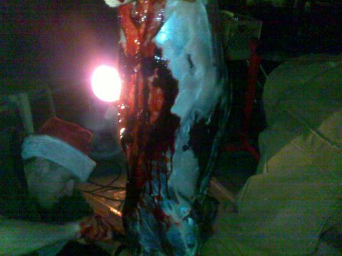 2006 Dodge 2500 - A gruesome scene with a hanging animal carcass and a person in a Santa hat, illuminated by a bright light.