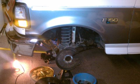1994 Ford F-150 - Front suspension and fender of a 1994 Ford F-150 XL undergoing maintenance, with parts laid out on the floor.