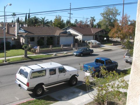 1968 Ford Mustang - A white SUV with a lifted suspension is parked on a residential street next to a blue pickup truck.