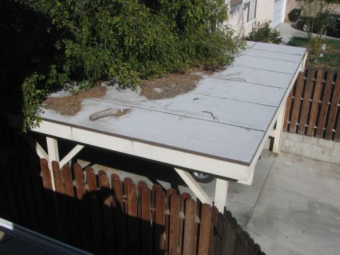 1968 Ford Mustang - A carport is covered by a large tree, with a wooden fence in the foreground.