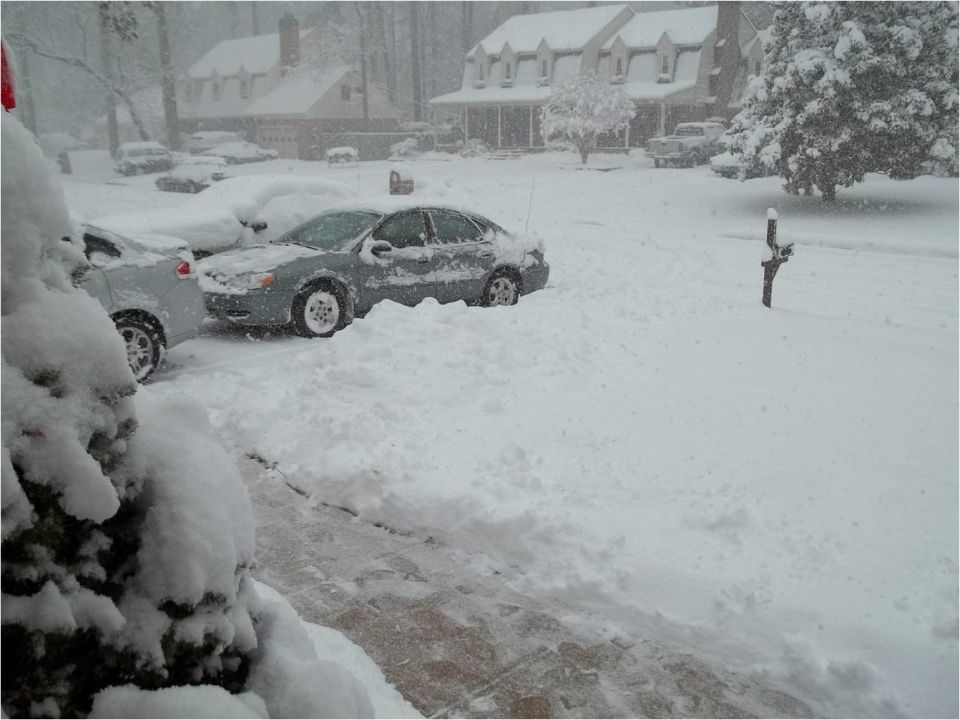 Several cars buried in snow on a residential street during a blizzard