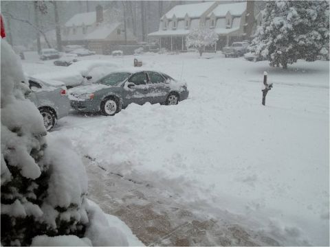 1972 Ford Ranchero - Multiple vehicles are stuck in deep snow on a street with houses in the background.
