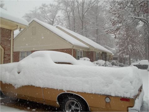 1972 Ford Ranchero - Side view of a gold/tan car-based pickup buried under roughly a foot of fresh snow in a residential driveway during a snowstorm, with only…