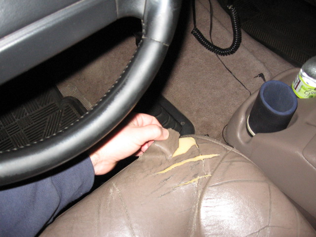 Torn tan leather seat exposing yellow foam beside a black steering wheel in a vehicle interior