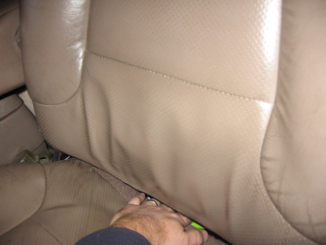 Tan perforated leather vehicle seat with a hand working underneath during a seat cover install.