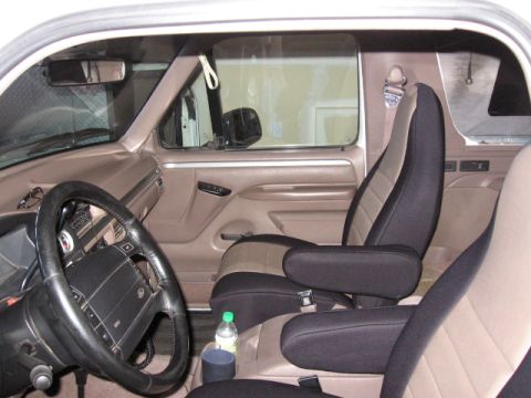 1995 Ford Bronco - The interior of a vehicle shows front seats with custom seat covers and armrests.