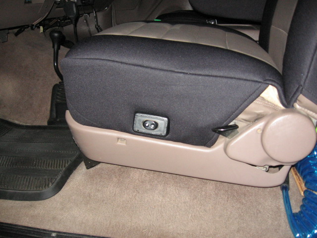 Vehicle seat with black cover over tan seat base and round recliner knob