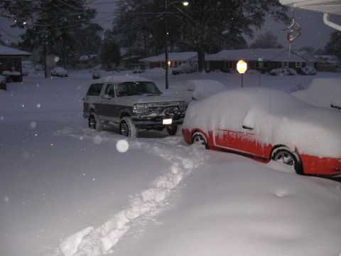 1994 Ford Bronco - A two-tone Ford Bronco navigates a snow-covered driveway, with another vehicle partially visible.
