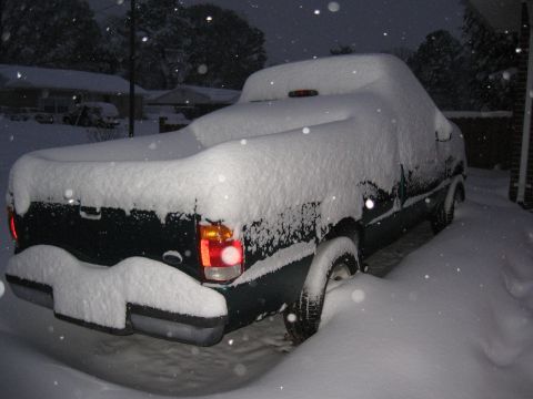 1994 Ford Bronco - A dark pickup truck is covered in snow during a winter storm.