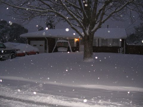 1994 Ford Bronco - A winter scene shows two vehicles covered in snow parked in front of a house during a snowfall.