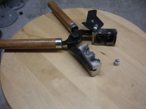 1996 Ford Bronco - A bullet mold with wooden handles is shown on a wooden surface, with a single bullet nearby.