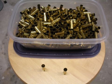 1996 Ford Bronco - A clear plastic container overflows with brass shell casings, with two casings resting on the wooden table in front.