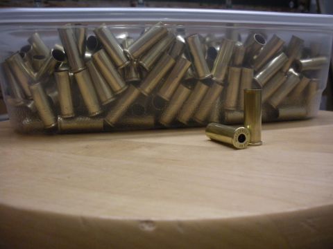 1996 Ford Bronco - A collection of brass shell casings fills a clear plastic container, with two casings resting on a wooden table in the foreground.